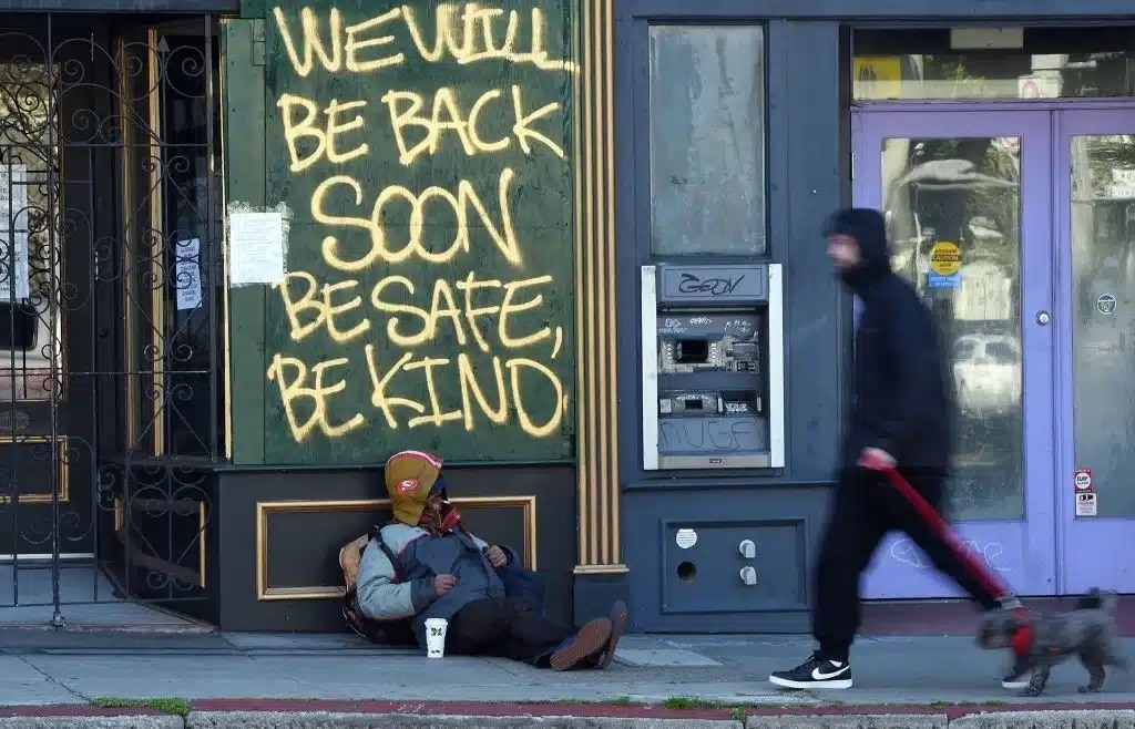 A homeless man sits on a California sidewalk